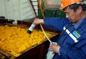 A worker in a Kazatomprom uniform is holding a radiation measuring device by a container of uranium.